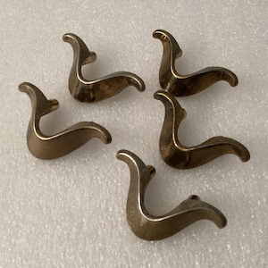 May include: Five vintage brass drawer pulls with a curved design. Each pull has a swan-like shape with a curved body and a raised, curved handle. The pulls are arranged on a white surface.