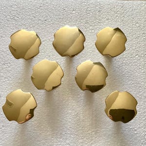 May include: Seven gold-toned metal cabinet knobs with a starburst design. The knobs are arranged in a semi-circle on a white surface.