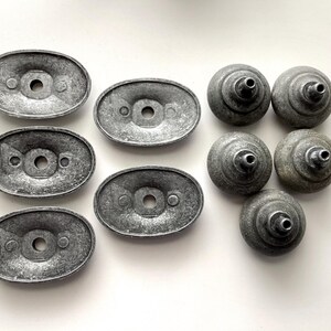 May include: A selection of vintage cabinet hardware, featuring oval backplates and round knobs. The metal components have a distressed, grey finish, giving a sense of age. Suitable for furniture restoration or DIY projects.