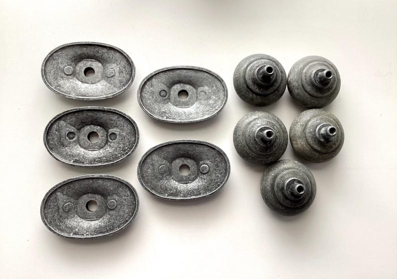 May include: A selection of vintage cabinet hardware, featuring oval backplates and round knobs. The metal components have a distressed, grey finish, giving a sense of age. Suitable for furniture restoration or DIY projects.