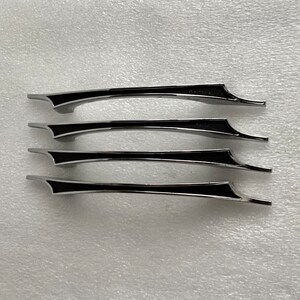 May include: Four cabinet handles with a sleek, modern design. Each handle is a polished silver color with a black accent in the center. The handles are curved and have a unique shape, perfect for adding a touch of elegance to any furniture piece.