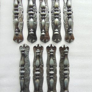 May include: Ten antique-style drawer pulls with a silver finish and a decorative design. The pulls have a textured surface and a slightly aged look.
