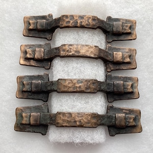 May include: Four metal drawer pulls with a dark bronze finish and a hammered texture. Each handle features a central arched bar with a rectangular base at both ends, secured by square brackets. The hardware has a weathered, aged appearance.