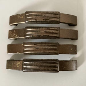 May include: Four antique bronze-toned cabinet pulls. Each pull features a rectangular center section with horizontal ridges and curved end pieces. The hardware shows signs of wear, with a distressed finish.