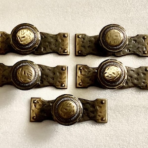 May include: Set of six antique brass cabinet knobs with a hammered finish and ornate round details. Each knob has a decorative design on the front.