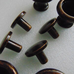 May include: A set of six antique bronze cabinet knobs. The knobs have a round base and a short, round stem. The knobs are in various positions on a white surface.