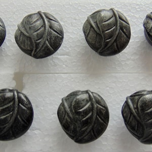 May include: Eight antique-style cabinet knobs with a leaf design. The knobs are round and made of a dark, metallic material with visible texture and detailing. The knobs are arranged in two rows of four.