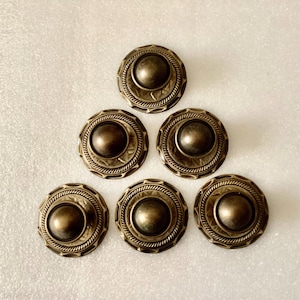 May include: Six antique bronze-colored buttons arranged in a triangular pattern. Each button features a central, raised dome surrounded by a decorative rope-like border and an outer patterned ring. The buttons have a vintage, aged appearance.