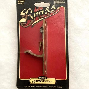May include: A solid brass door edge pull mounted on a black and red display card. The packaging features the text DOOR EDGE PULL, solid Brass, IVES ARTISAN Collection, and 1983 H.B. IVES, A HARROW COMPANY, NEW HAVEN, CT 06508 with model numbers.