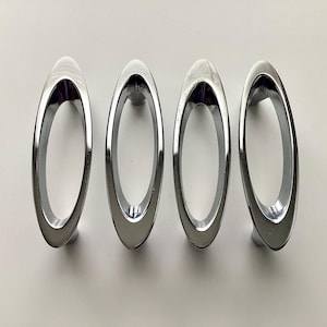 May include: Four polished chrome oval cabinet pulls. Each pull has a smooth, reflective surface and a rounded, elongated shape. The pulls are designed for easy gripping and add a modern touch to furniture or cabinetry.