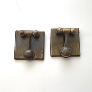 May include: Two antique brass drawer pulls. Each pull features a square backplate with a central stem and a round knob at the end. The pulls have a vintage, aged appearance with a warm, golden-brown color.
