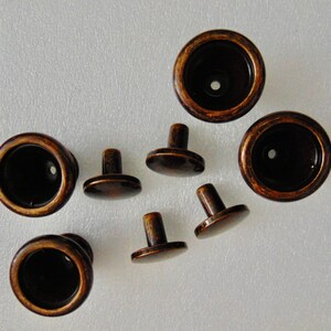 May include: A set of eight antique-style cabinet knobs. The knobs are made of metal and have a dark brown finish. Some of the knobs have a round shape, while others have a more traditional knob shape with a small post.