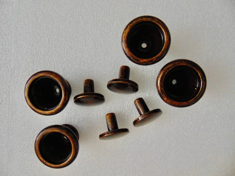 May include: A set of eight antique-style cabinet knobs. The knobs are made of metal and have a dark brown finish. Some of the knobs have a round shape, while others have a more traditional knob shape with a small post.