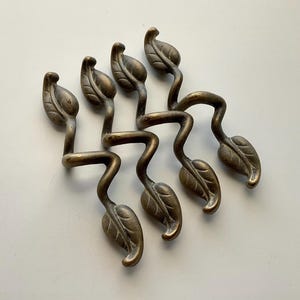 May include: Six antique brass leaf-shaped drawer pulls. Each pull features a stylized leaf at the end of a curved stem. The brass has a warm, aged patina. The pulls are arranged in a cluster, suggesting they are decorative hardware.