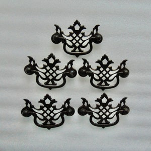 May include: A set of five dark metal drawer pulls featuring an ornate, openwork lattice design with a central diamond pattern and curved, decorative edges. Each pull includes a swinging handle attached to two circular mounting points on the sides.