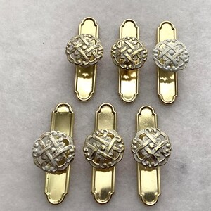 May include: A set of six drawer pulls, each featuring a rectangular gold-tone metal backplate with rounded ends and a circular, openwork knob with a silver-tone finish. The knobs display a woven, lattice-like pattern with a central dot.