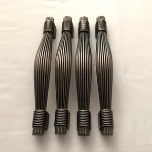 May include: Four antique bronze cabinet pulls. Each pull has a ribbed, curved handle and is accented with a coiled design at the top and bottom. The pulls are designed for easy installation and add a vintage touch to furniture.