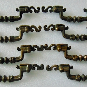 May include: Eight antique brass cabinet pulls with ornate scrollwork and a decorative center. The pulls are arranged in four rows of two.