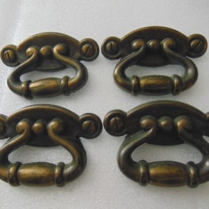 May include: Four antique brass cabinet pulls with ornate details. Each pull has a rounded rectangular shape with a decorative loop handle.