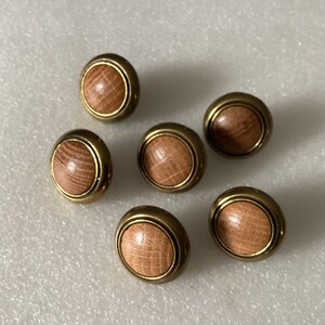 May include: Six round wooden buttons with a brass rim. The buttons have a light brown wood grain pattern.