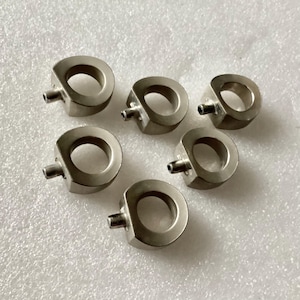 May include: Six silver metal rings with a small hole on one side. The rings are all the same size and shape.