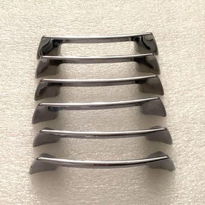 May include: Six dark gray cabinet pulls with a curved bar design. The pulls have a metallic finish and are arranged in parallel rows. The handles are likely for drawers or cabinet doors.