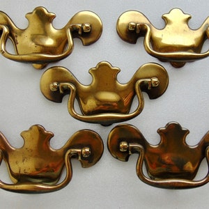 May include: Five antique brass cabinet pulls with a decorative, ornate design. Each pull has a curved handle and a decorative top.