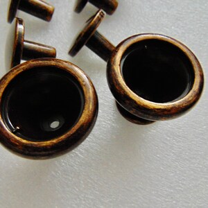 May include: Close-up of two antique brass cabinet knobs with a round, slightly raised,  rim and a small hole in the center. The knobs have a dark brown patina.