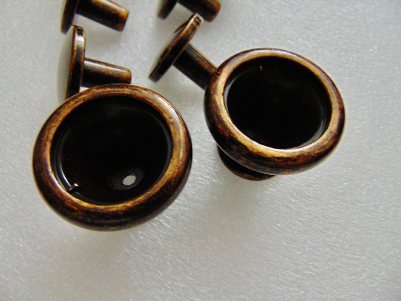 May include: Close-up of two antique brass cabinet knobs with a round, slightly raised,  rim and a small hole in the center. The knobs have a dark brown patina.