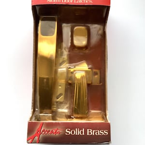 May include: A new, packaged door latch set in a cardboard box. The set includes a gold-colored door handle and other hardware. The box has red and brown accents with the text "Replaces Most Push-Button Storm Door Latches" and "Accent Solid Brass".
