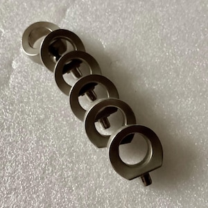 May include: A set of six silver metal rings with a small screw on the bottom of each ring. The rings are stacked on top of each other.