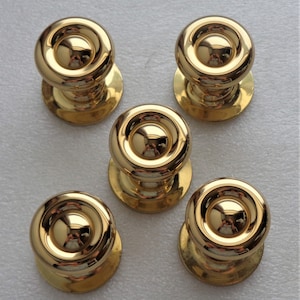 May include: Five shiny, gold-colored cabinet knobs. Each knob has a rounded top with a circular design and a small, circular base. The knobs reflect light, creating a bright and polished appearance.