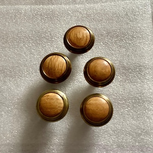 May include: Five round wooden knobs with a brass rim. The knobs have a light brown wood grain pattern.