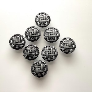 May include: Eight silver-toned cabinet knobs arranged on a white surface. Each knob has a woven basket design with a scalloped edge. The knobs are round and appear to be made of metal.