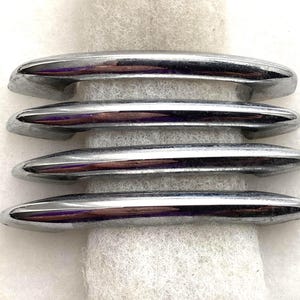 May include: Four polished chrome cabinet pulls arranged horizontally. Each handle features a smooth, elongated, and slightly curved design with a reflective metallic finish. The hardware pieces are uniform in shape and size, showcasing a sleek, modern appearance with rounded ends and a consistent silver-toned surface throughout the set.