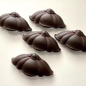 May include: Five dark brown, flower-shaped cabinet knobs arranged on a white surface. Each knob has a rounded center and petal-like edges, creating a decorative and functional hardware element.