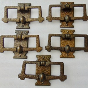 May include: A set of five bronze-toned metal drawer pulls featuring a rectangular backplate with a hammered texture and a central vertical bar. Each pull has a rectangular swinging handle attached to the center, finished in a dark metallic patina.