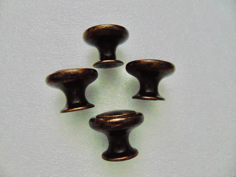 May include: Four antique bronze cabinet knobs with a round top and a short, round base.