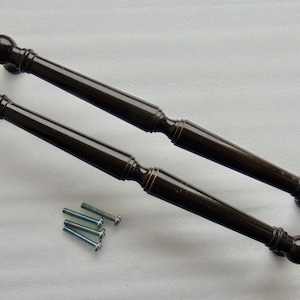 May include: Two dark brown cabinet pulls with decorative ends and a central, slightly wider section. The pulls are accompanied by several silver screws, suggesting they are ready for installation. The hardware has a classic, elegant design.