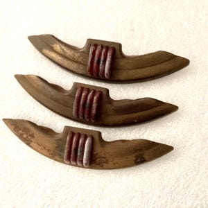 May include: Three vintage bronze-toned decorative pieces. Each has a curved, boat-like shape with a central, rectangular section in a contrasting reddish-brown color. The pieces appear to be made of metal and have a slightly aged appearance.