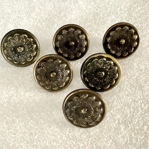 May include: Six antique brass-colored cabinet knobs with a floral design. Each knob is round with a raised, detailed flower pattern in the center and around the edges. The knobs have a vintage, aged appearance.