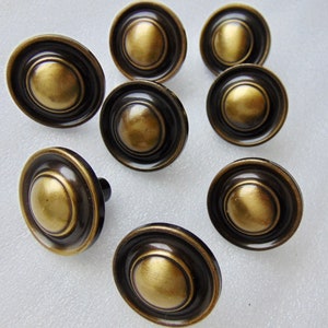 May include: Eight antique gold cabinet knobs with a black ring around the edge. The knobs have a raised, rounded center.