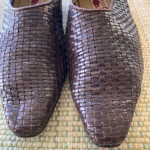Puede incluir: Primer plano de un par de zapatos de cuero marr&oacute;n tejido. Los zapatos tienen un dise&ntilde;o sin cordones con punta puntiaguda. El patr&oacute;n tejido cubre todo el zapato, creando una apariencia texturizada. El interior del zapato es visible, con una etiqueta.