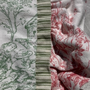 May include: A textile piece featuring a white fabric with a green toile print of figures and trees, joined by a vertical strip of green and white striped fabric to a section of white fabric with a red toile print of floral and botanical patterns.