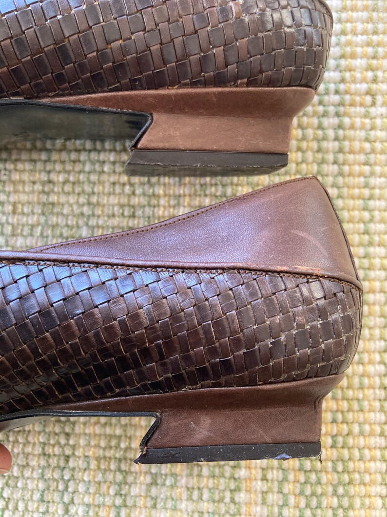 Puede incluir: Primer plano de dos zapatos de cuero marr&oacute;n. Los zapatos tienen un patr&oacute;n tejido en la parte superior y un tac&oacute;n bajo. Las suelas son de color marr&oacute;n oscuro y los zapatos parecen desgastados.