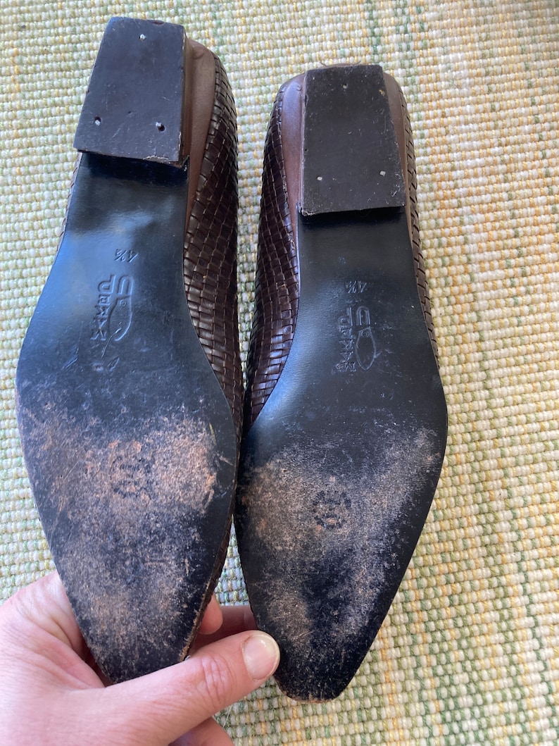 Puede incluir: Par de bailarinas de cuero marr&oacute;n tejido con puntera cuadrada. Las suelas son oscuras con desgaste y los tacones son de color marr&oacute;n oscuro. Los zapatos son de talla 4 1/2.