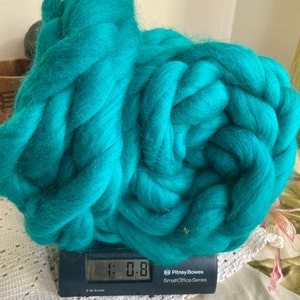Könnte beinhalten: Ein großes, dickes Knäuel aus leuchtend türkisfarbener Kammwolle, das auf einer schwarzen Digitalwaage liegt. Das Display der Waage zeigt ein Gewicht von 0,476 Kilogramm an. Die Wolle hat eine weiche, flauschige Textur und ist dicht gewickelt.