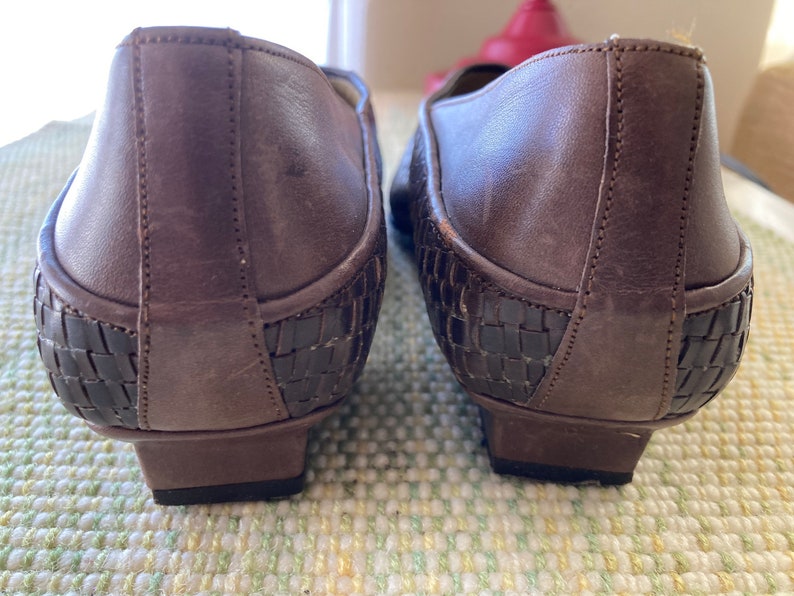 Puede incluir: Un par de zapatos de cuero marr&oacute;n con un dise&ntilde;o tejido en el tal&oacute;n. Los zapatos tienen un tac&oacute;n bajo y una punta redondeada. El cuero parece envejecido, d&aacute;ndoles un aspecto vintage. Zapatos para uso diario.
