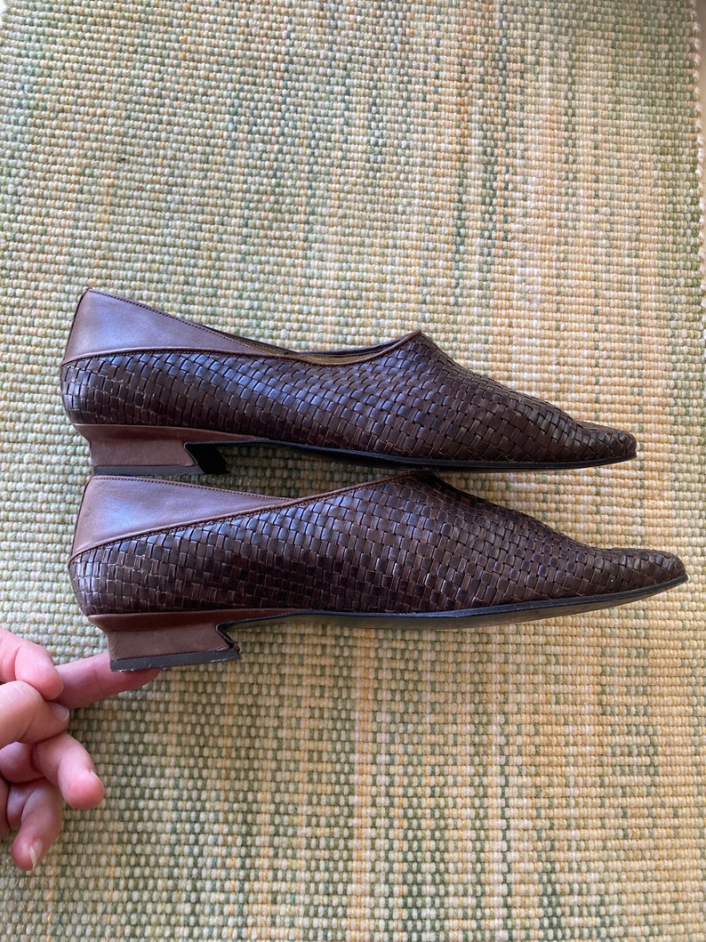 Puede incluir: Un par de zapatos planos de cuero marr&oacute;n tejido con puntas puntiagudas. Los zapatos tienen un tac&oacute;n bajo y un ribete de cuero marr&oacute;n en contraste. El patr&oacute;n tejido crea una apariencia texturizada.