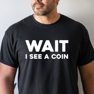 May include: A black t-shirt with white text that reads "WAIT I SEE A COIN".